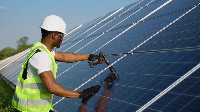 African american engineer in safety helmet and uniform at solar power station installing solar panels. Green energy.