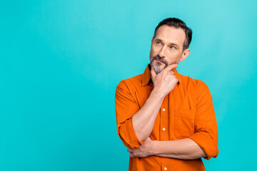Photo of serious intelligent guy wear orange shirt arm chin looking empty space isolated teal color background