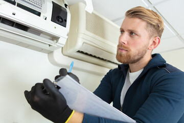 male technician holding clipboard looking at air conditioner