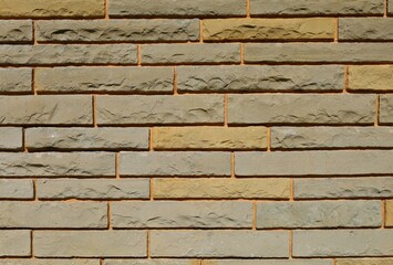 Stone wall made of elongated bricks of gray and yellow rocks on orange colored concrete. Background and texture.