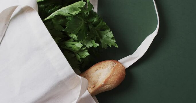 Video of white canvas bag with parsley, kale and baguette, copy space on green background