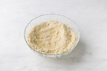 A glass bowl of grated butter with flour on a light gray background. Cooking delicious homemade pastries, step by step, cooking step