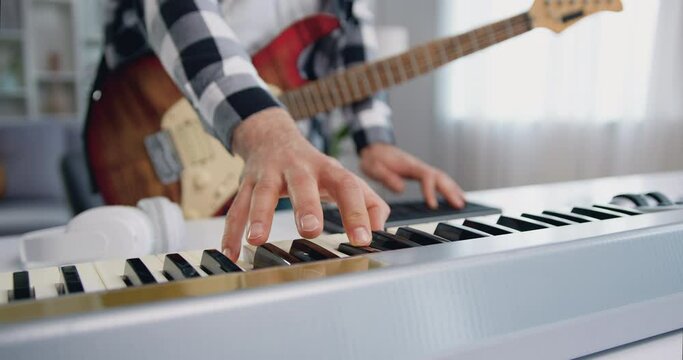 Close up of male hands playing midi piano keyboard and synthesizer in home studio. Musician recorded his composition in a home music studio using professional instruments