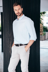Handsome confident stylish hipster lambersexual model. Modern man dressed in white shirt and trousers. Fashion male posing in the street urban background. Outdoors
