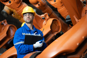 Industrial engineer examining robotic arm in heavy metalworking factory workshop. Huge robot arm...