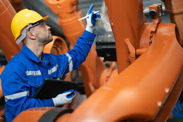 Industrial engineer examining robotic arm in heavy metalworking factory workshop. Huge robot arm...