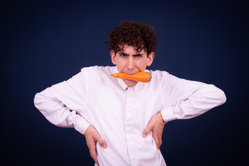 Vegetarianism. Funny emotional guy eats carrots. Student posing on a blue background.