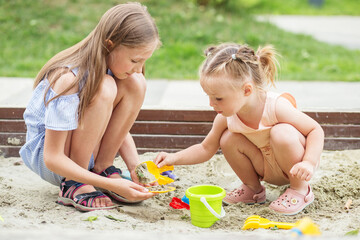 Girl and baby playing on sandbox. Toddler playing with sand molds and making mudpies.
