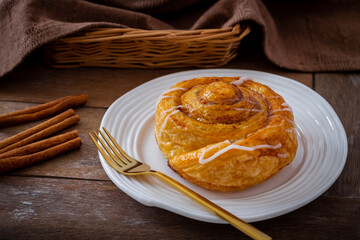 Cinnamon roll bun on white plate and cinnamon sticks on wooden table