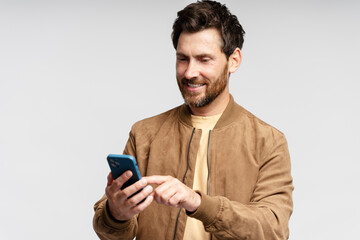 Portrait of smiling bearded man holding mobile phone, reading text message, communication online isolated on gray background. Handsome guy shopping online, choosing on website