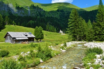 Obraz premium Muritzen stream and a alpine pasture with a wooden lodge and a chapel behind and mountain above at Hintermuhr, Austria