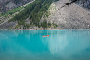 Couple canoeing in a glacial Moraine lake surrounded by mountains