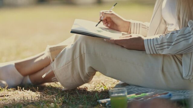 A woman sitting in the park holding a painting brush against the notebook