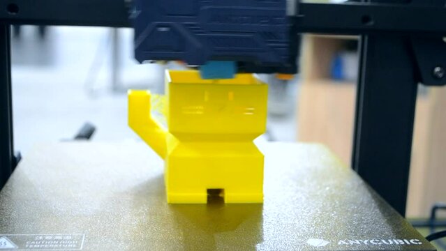 3D printer printing prototype of toy from molten plastic. Process of creating prototype model of toy on 3D printer from yellow melted plastic close-up. Additive new printer technology. Modern printing