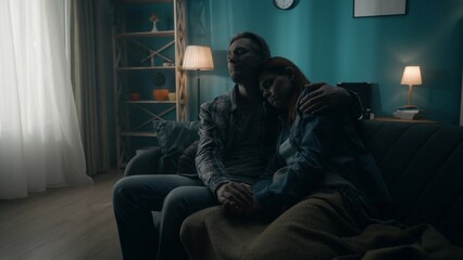 A couple is sitting on a sofa in a dark room close up. A man holds a woman by the hand, hugs. Support for the couple, joint problem solving, reconciliation and understanding in relationships.