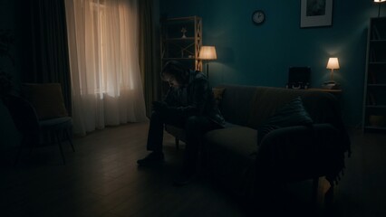 Smartphone addiction and depression. A man sits in a room in total darkness with a phone in his...