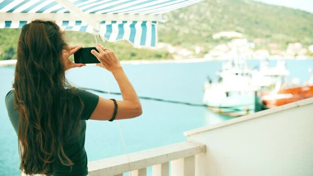 A woman takes pictures of the beautiful Mediterranean scenery with her smartphone from the seaview terrace