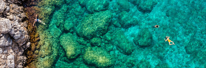 Aerial view of a young couple snorkeling above coral reef reaching deeper parts of the crystal clear water, Rhodes, Greece. Aerial drone view of a couple snorkeling swimming in crystal clear water.