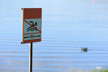 Information sign "swimming is prohibited", a sign near the lake on a summer day
