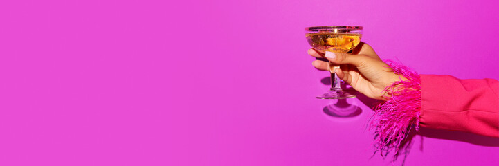 Female hand holding glass with light summer sparkling wine cocktail on bright violet background.