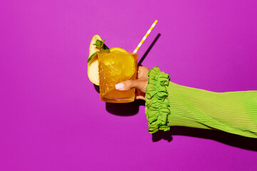 Hand holding glass of screwdriver cocktail with colorful tube over bright studio background. Pop art photoshoot.