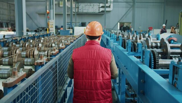 Shot back industry engineer man wearing safety uniform and hard hat walk checks production processes in factory. Look around. Inspector in warehouse.