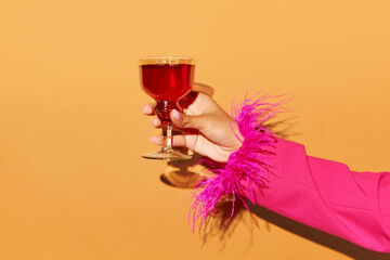 Hand holding high glass with Rob Roy cocktail over light orange background. Copy space for ad.