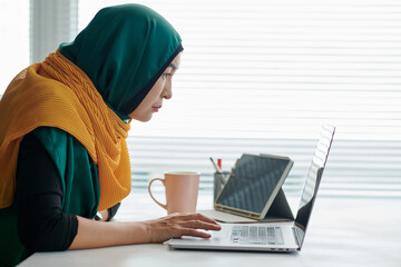 Mature muslim businesswoman in hijab reading e-mail from client om laptop screen