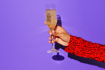 Lady's hand holding glass of shampange on violet background. Contemporary pop art image.