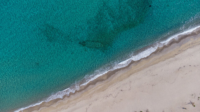The Livadi Beach at the Ikaria island in a quiet summer day with blue clear water and nature behind, Ikaria, Greece. Little beach lagoon next to the shore.