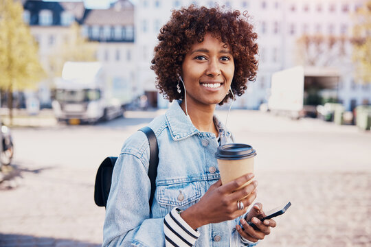 Smiling woman having coffee and listening to music on headphones in the city