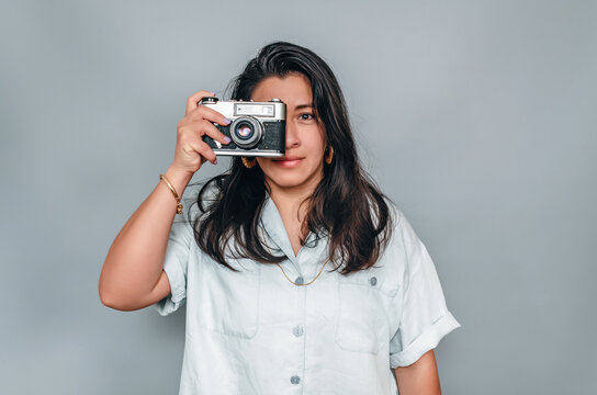 Latin American woman taking photos in the studio. Woman with a camera. Gray background.