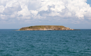 Fototapeta na wymiar Wild uninhabited island in the sea and thick white clouds in the sky