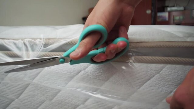 Man uncovering mattress with scissors in a bedroom