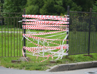 Red and white restrictive tape closes the passage in the broken metal fence