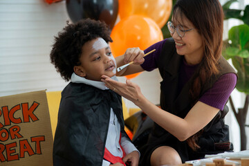 Mother and son in Halloween costumes having fun with makeup, mother paints a pattern on her son's face with a paintbrush. happy halloween together