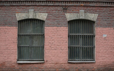 Fototapeta na wymiar Two barred windows in an old red brick wall