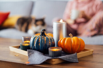 Autumn, fall cozy mood composition for hygge home decor. Small pumpkins, burning candles on tray...