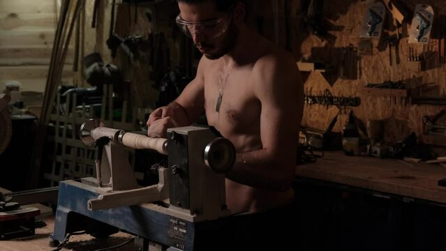 A young guy with an athletic physique is engaged in carpentry work in the workshop.