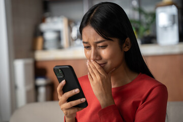 Beautiful asian woman looking to phone and crying. She was shocked with the bad news she received.