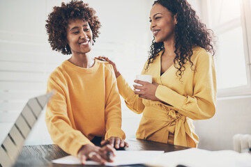 Two businesswomen laughing while working together at an office table
