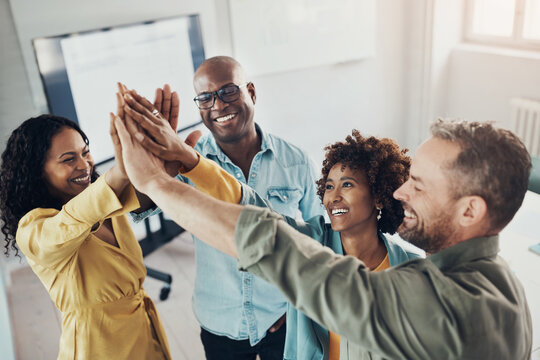 Diverse team of laughing businesspeople standing with their hands raised together