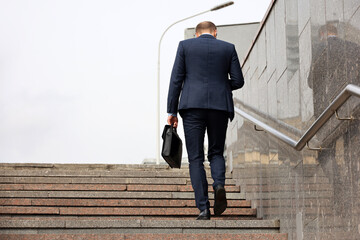 Man in a business suit with briefcase climbing steep stairs. Concept of career, success, moving to the top, official or businessman