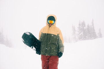 Portrait of snowboarder with board wearing mask in snowy winter landscape outdoors