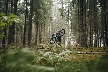 Lone rider carrying his mountain bike along a forest trail