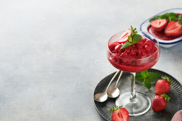 Strawberry granita or fresh berry sorbet in glass on old  grey table background. Texture of ice cream or sorbet. Ice cream with strawberry and mint. Sorbet recipe. Summer treat. Selective focus.