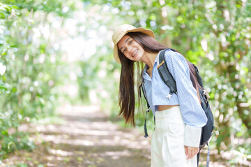 Pretty young Asian girl smiling face. Backpacking to study nature in the forest that is open for people to come and admire nature. woman in a hat protects herself from scorching sun while taking walk