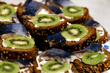 A delectable sandwich with herring and kiwi fruit on a slice of black bread. Enjoy this healthy treat with fresh herring fish on a dark background. Out of focus