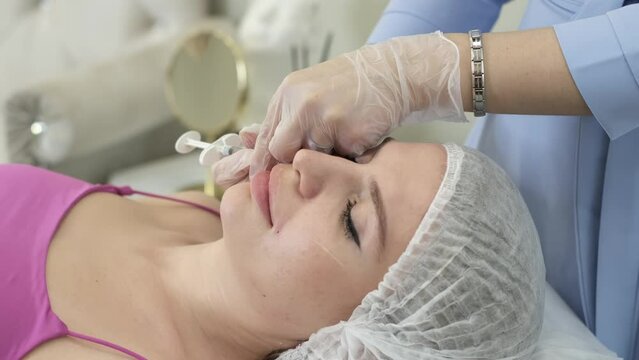 clip shows intensive facial skin care in a beauty clinic: a doctor injects filler into the patient's nasolabial folds. The purpose of the procedure is to improve facial contours and combat signs of