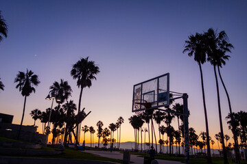 Silhouettes in the colorful sunset sky of palm trees, basketball hoops, and other things at Venice Beach in Los Angeles, California.  © Adam